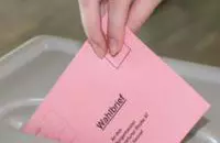 Eine Hand wirft einen Stimmzettelumschlag in eine Wahlurne.